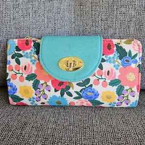 May include: A turquoise and floral patterned wallet with a gold clasp. The wallet has a floral pattern with pink, yellow, blue, and green flowers.