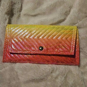 May include: A pink, orange, and yellow ombre quilted wallet with a single snap closure.