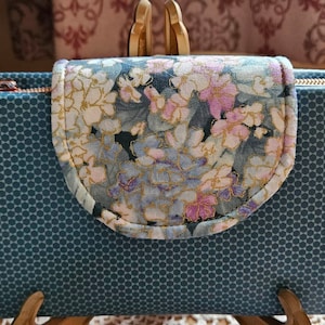 May include: A teal blue zippered wallet with a floral pattern on the flap. The wallet has a honeycomb pattern on the exterior.