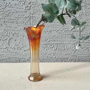 May include: An iridescent orange and clear glass vase with a flared top and a detailed base. The vase is holding a sprig of green eucalyptus leaves. The vase is approximately 10 inches tall.