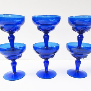 May include: Set of six cobalt blue glass champagne coupes with a fluted design. The glasses are stacked in pairs, with the top two glasses upside down.