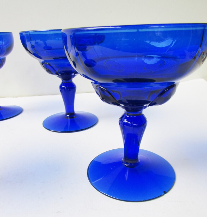 May include: Set of three cobalt blue glass stemmed cocktail glasses. The glasses have a fluted design and a wide bowl.