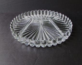 May include: Clear glass serving dish with a divided design. The oval-shaped dish features a central square section and radiating lines. The rim has a scalloped edge. A classic piece for serving appetizers or snacks.