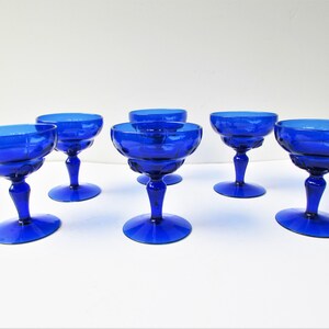 May include: Set of six cobalt blue glass champagne coupes. The coupes have a fluted design and a stemmed base.