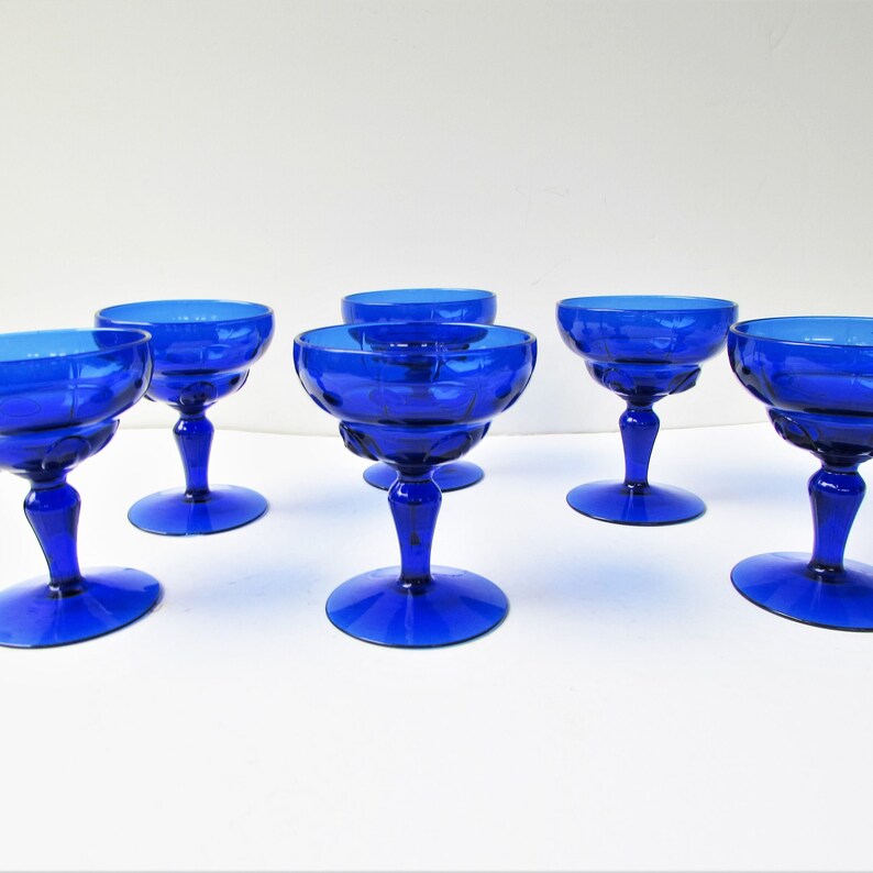 May include: Set of six cobalt blue glass champagne coupes. The coupes have a fluted design and a stemmed base.
