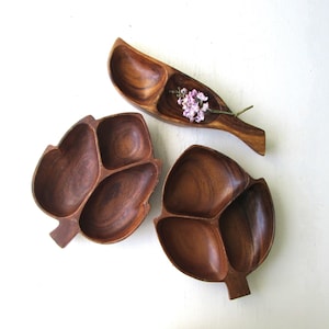 May include: Three wooden serving dishes, two are leaf-shaped with three sections each, and one is a long, narrow, curved shape with three sections. The dishes are made of dark brown wood.