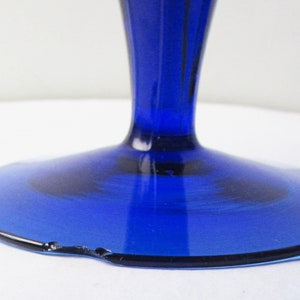 May include: Cobalt blue glass pedestal with a wide, round base. The base has a slight chip on the edge.