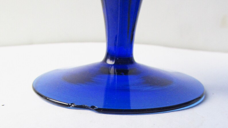 May include: Cobalt blue glass pedestal with a wide, round base. The base has a slight chip on the edge.