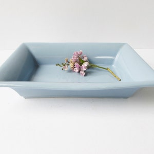 May include: A light blue rectangular ceramic dish with a sprig of pink flowers on top.