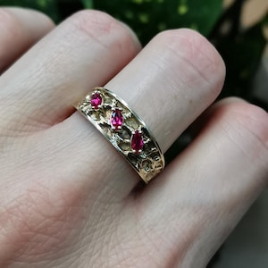May include: Gold band ring with three red gemstones set in a textured design.