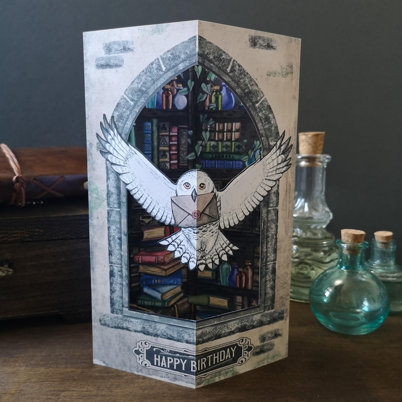 Może przedstawiać: Ręcznie robiona kartka urodzinowa z efektem 3D przedstawiająca białą sowę niosącą list na tle biblioteki. Karta zawiera napis "HAPPY BIRTHDAY" na dole, z efektem szczeg&oacute;łowym i warstwowym.