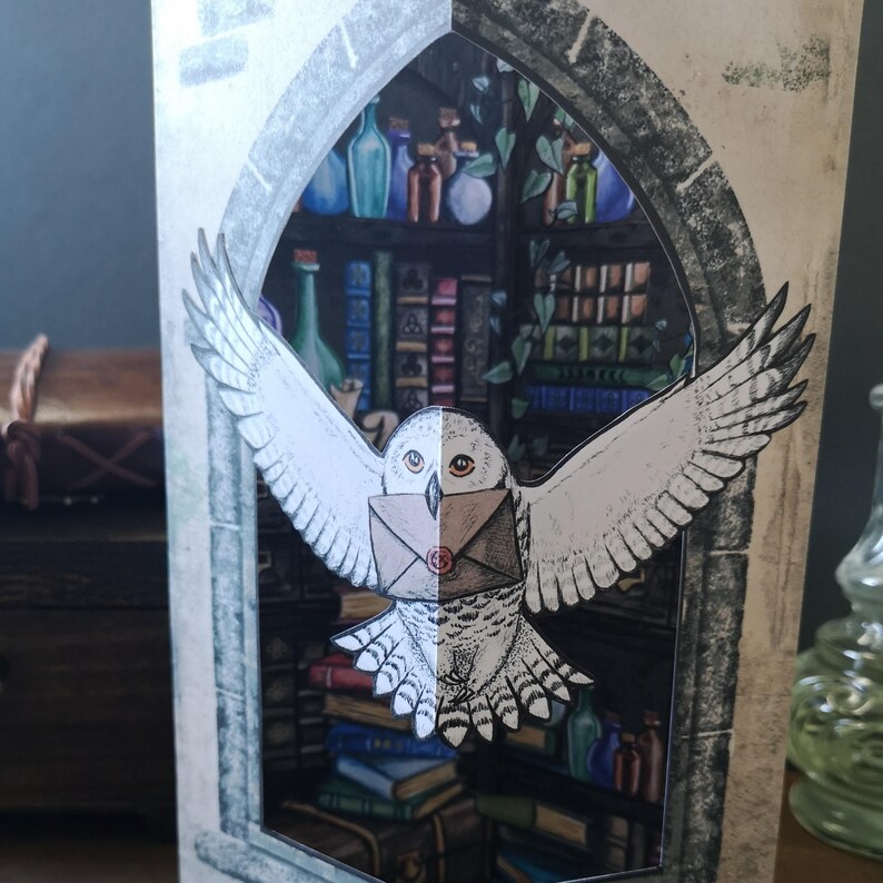 Może przedstawiać: Wyskakująca kartka z życzeniami przedstawiająca białą sowę niosącą list, na tle biblioteki z butelkami z eliksirami i książkami. Skrzydła sowy są rozłożone, a karta ma warstwową konstrukcję.