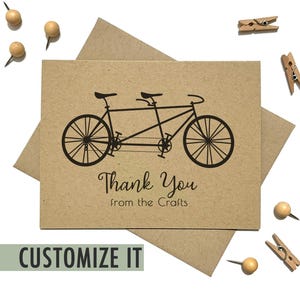 May include: A rectangular tan card featuring a black graphic of a tandem bicycle. Below the bicycle, the text reads Thank You in a cursive script and from the Crafts in a simple sans-serif font. The card is placed on a matching tan envelope.