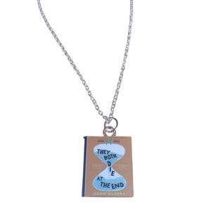 May include: A silver chain necklace with a pendant featuring the book cover of "They Both Die at the End" by Adam Silvera. The cover is brown with a blue hourglass graphic and white text.