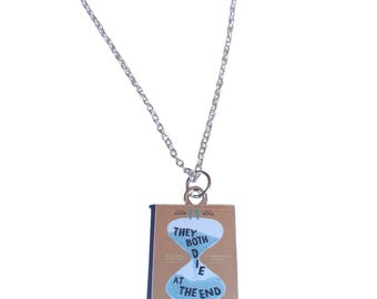 May include: A silver chain necklace with a pendant featuring the book cover of "They Both Die at the End" by Adam Silvera. The cover is brown with a blue hourglass graphic and white text.