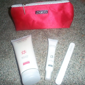 May include: A red zippered cosmetic bag with a silver ONSEN logo plate, a white tube of ONSEN body lotion, a smaller white tube of ONSEN cream, and a long, thin white nail file. All items feature the ONSEN brand name printed in black text.
