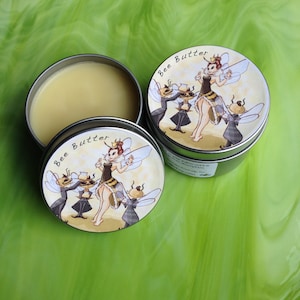 May include: Two silver tins of bee butter with a whimsical illustration of a bee fairy with wings and a crown, surrounded by bees. The text on the tin reads "Bee Butter".