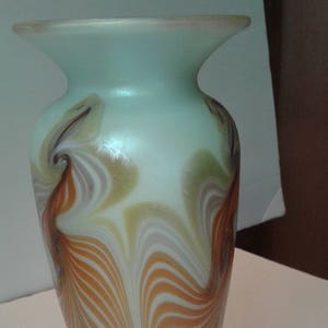 May include: A tall, iridescent glass vase with a swirling pattern of brown, white, and green. The vase has a wide mouth and a narrow base.