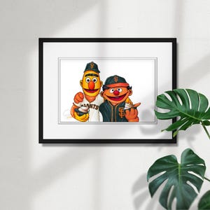 Op de afbeelding: Een ingelijste prent met twee stripfiguren in honkbaltenue. Eén figuur draagt een Giants honkbalpet en -shirt, de ander draagt een Giants honkbalpet en -shirt. Beide figuren houden een snack vast.