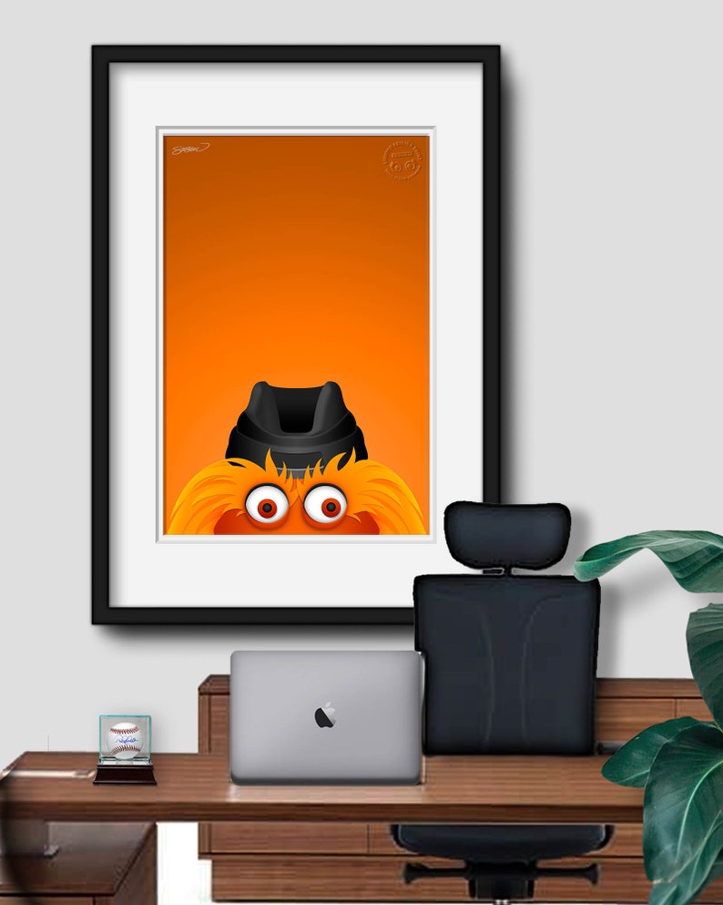 May include: A framed illustration of the mascot for the Baltimore Orioles, a furry orange creature with a black hat and large eyes, against an orange background.