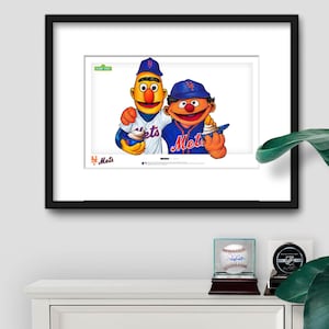 Puede incluir: Impresi&oacute;n enmarcada con Bert y Ernie de Barrio S&eacute;samo con uniformes de b&eacute;isbol de los Mets de Nueva York. Bert lleva una camiseta a rayas, Ernie una azul. El logotipo de los Mets es visible, junto con el logotipo de Barrio S&eacute;samo.
