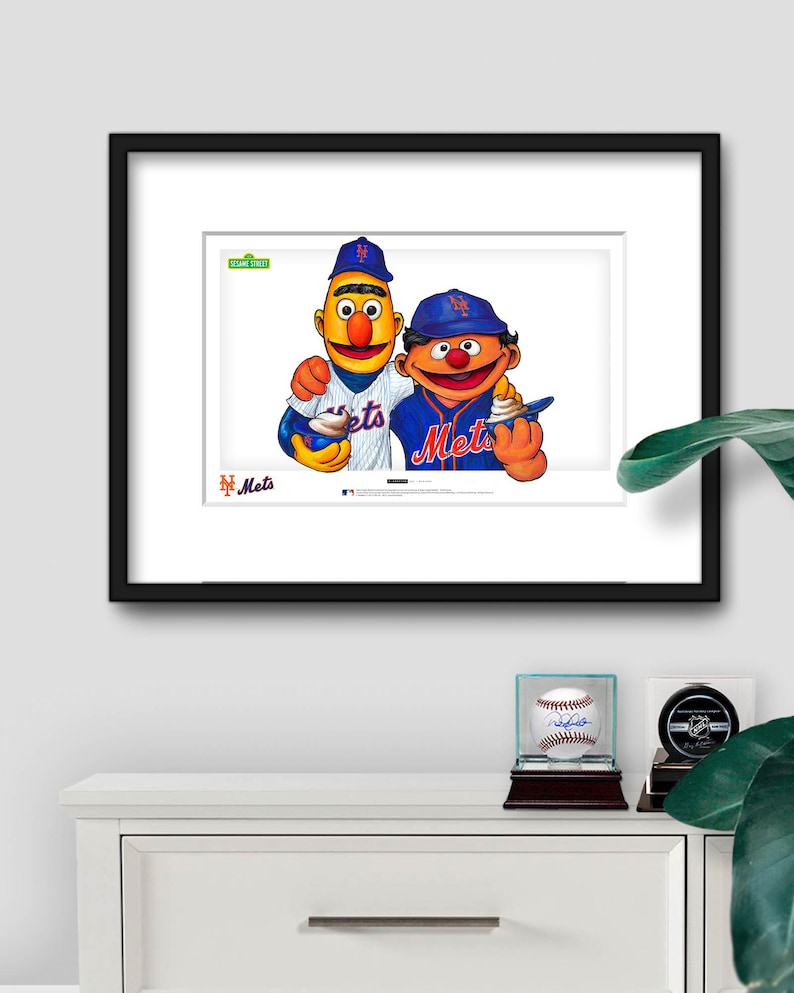 Puede incluir: Impresi&oacute;n enmarcada con Bert y Ernie de Barrio S&eacute;samo con uniformes de b&eacute;isbol de los Mets de Nueva York. Bert lleva una camiseta a rayas, Ernie una azul. El logotipo de los Mets es visible, junto con el logotipo de Barrio S&eacute;samo.