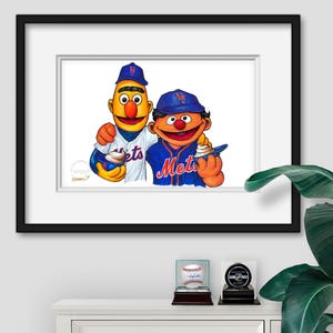 Puede incluir: Una impresi&oacute;n enmarcada con dos personajes de dibujos animados con uniformes de b&eacute;isbol, uno con una camiseta azul de los Mets y el otro con una camiseta a rayas. La impresi&oacute;n se exhibe en un gabinete blanco con una pelota de b&eacute;isbol y un disco de hockey en vitrinas.