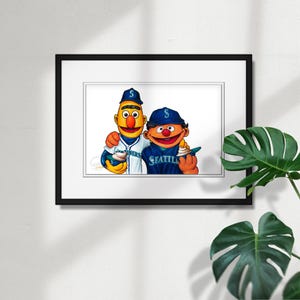 May include: A framed print featuring two Sesame Street characters in Seattle Mariners baseball uniforms. One character wears a blue cap and jersey with "Seattle" on it. The other wears a Mariners jersey. Both characters hold ice cream cones.