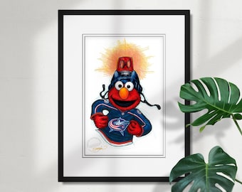 May include: Framed artwork featuring a cartoon character in a hockey jersey. The character is red with large eyes and is wearing a hockey helmet and jersey with the Columbus Blue Jackets logo. The background is a bright yellow burst.