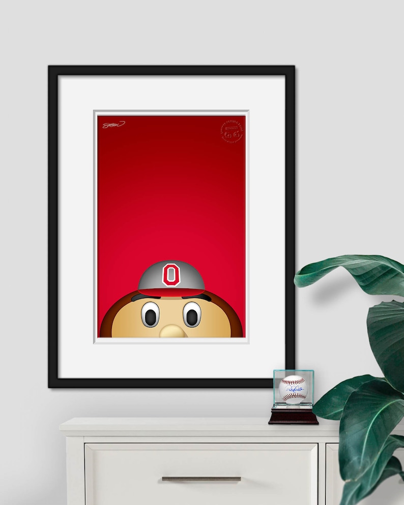 May include: A framed illustration of a cartoon mascot wearing a red and white baseball cap with a large "O" on the front. The mascot has brown hair, a brown face, and large eyes. The background is red.