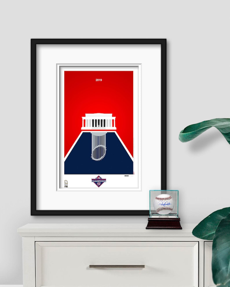 Puede incluir: Una impresi&oacute;n enmarcada de un estadio de b&eacute;isbol con un esquema de color rojo, blanco y azul. El estadio se representa como una silueta con un trofeo de b&eacute;isbol en el centro. El texto "2019" y "CHAMPIONS" es visible en la impresi&oacute;n.