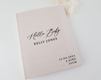 May include: A beige linen baby memory book with the text "Hello Baby" in a cursive font and "KELLY JONES" printed below. The date "13.04.2023", weight "3.45KG", and length "55CM" are printed on the bottom right corner.