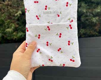 May include: White fabric pouch with a cherry pattern. The pouch has a small pocket on the front and a zipper closure. The text "BOBBIN TAILS" is printed on the front. The cherries are red with green stems and leaves.