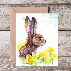 May include: Watercolor painting of a brown hare with large ears, looking to the right. The hare is surrounded by yellow daffodils.