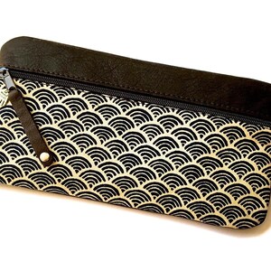 Könnte beinhalten: Eine schwarze und cremefarbene Reißverschlusstasche mit geometrischem Muster. Die Tasche hat eine schwarze Lederklappe mit Reißverschluss.