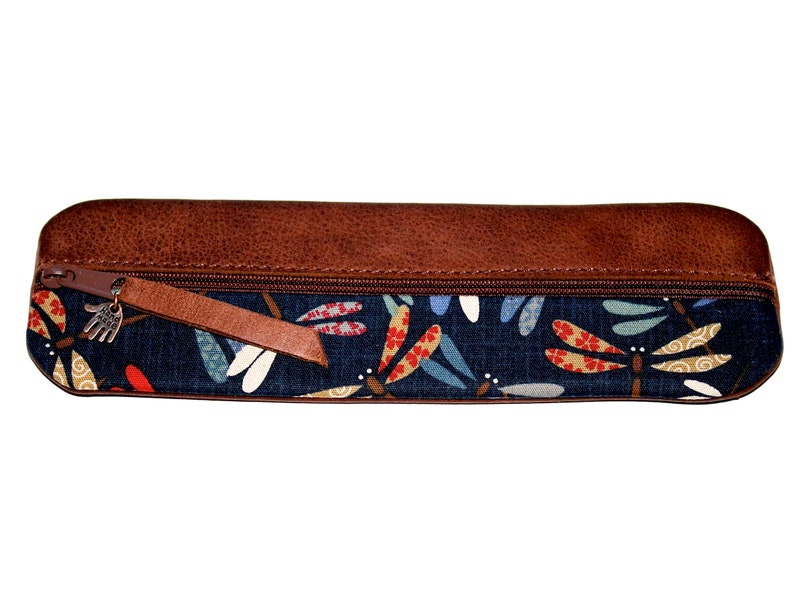 May include: A brown leather zippered pencil case with a blue fabric lining featuring a dragonfly pattern. The zipper pull has a small metal charm.