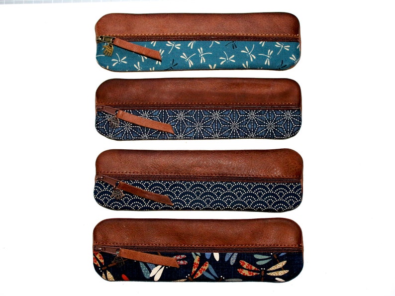 May include: Four brown leather pencil cases with different blue and white patterned fabric lining. The fabric patterns include dragonflies, geometric shapes, and waves.