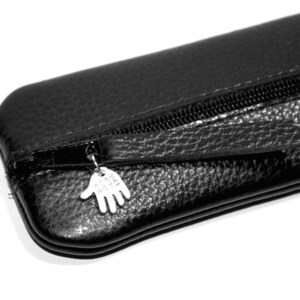 May include: Black leather pencil case with a zipper closure and a silver charm in the shape of a hand.