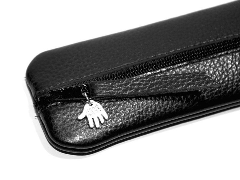 May include: Black leather pencil case with a zipper closure and a silver charm in the shape of a hand.