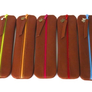 May include: Five brown leather pencil cases with different colored zippers. The zippers are lime green, orange, pink, red, and blue.