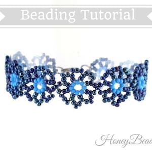 以下が含まれることがあります： 青と黒の雪の結晶のデザインのビーズブレスレット。ブレスレットは小さなビーズで作られており、雪の結晶の繰り返しパターンが特徴です。