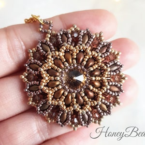 May include: A gold and brown beaded pendant with a clear crystal in the centre. The pendant is in the shape of a flower with multiple layers of beads.