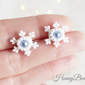 May include: A pair of white snowflake earrings with a light blue pearl in the center of each snowflake.