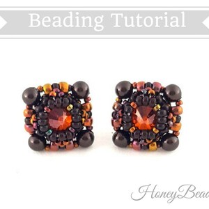 以下が含まれることがあります： 濃い茶色、オレンジ、赤の色合いの正方形のイヤリングのペア。イヤリングは、中央に赤い宝石を、その周りを小さなビーズで囲んでいます。