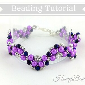 以下が含まれることがあります： 波打つデザインの紫と銀のビーズブレスレット。ブレスレットは小さな丸いビーズとクリスタルビーズで作られています。ブレスレットは白い背景の上にあります。