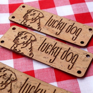 Könnte beinhalten: Drei braune Korkstoff-Etiketten mit einer Hundesilhouette und dem Text "lucky dog" auf jeder.