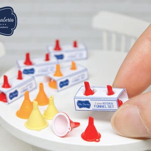 Op de afbeelding: Miniatuurkeukentrechters in rood, oranje en geel, met een wit en blauw doosje met het opschrift "2 piece Kitchen Funnel Set". De trechters staan op een wit oppervlak. De afbeelding bevat de tekst "Mini Fanaberia".