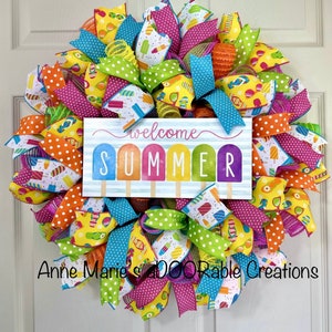 May include: A colorful summer wreath with a sign that says "Welcome Summer" with popsicle graphics. The wreath is made with various ribbons and mesh in shades of pink, green, blue, yellow, and orange.