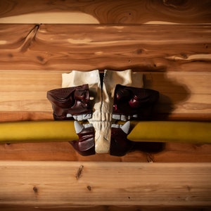 May include: A white skull mask with red and black accents is holding a gold katana sword in its teeth. The mask is mounted on a wooden wall.