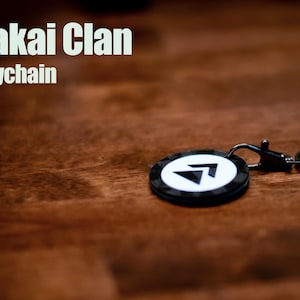May include: A black and white keychain with a white arrow logo and the text "Sakai Clan Keychain".